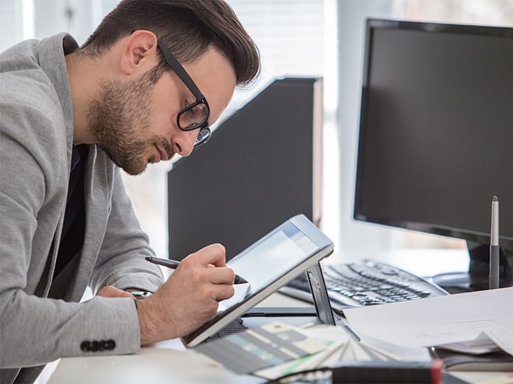 A designer working on a tablet in at his office desk.