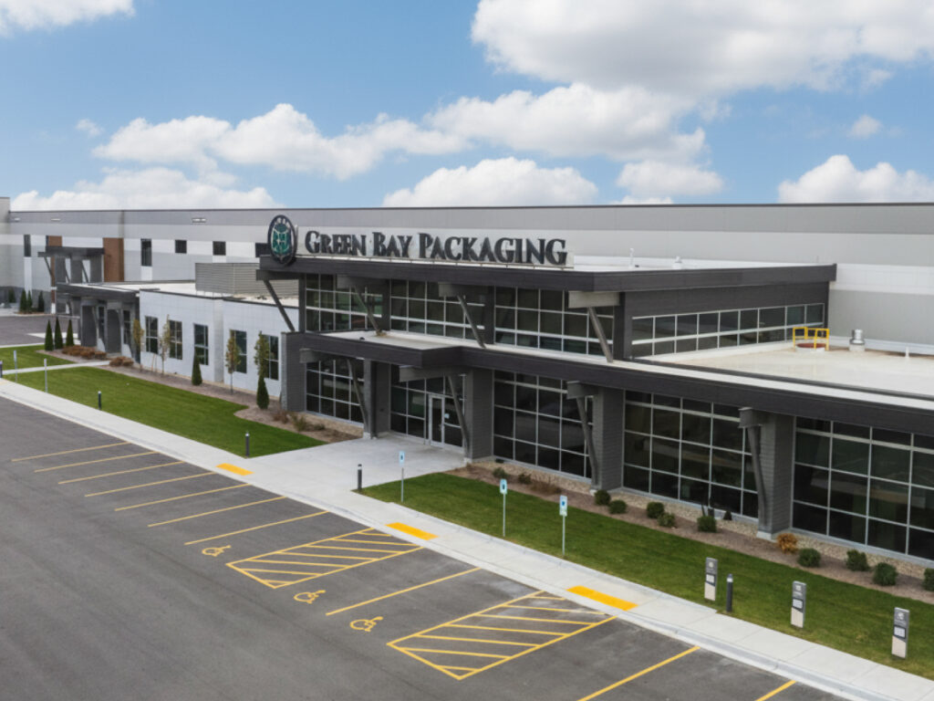 Exterior view of Green Bay Packaging's Great Lakes Division manufacturing facility with modern architecture, large glass windows, and company signage under a blue sky with clouds